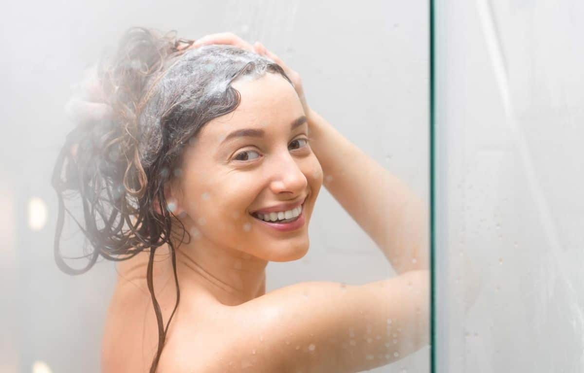 Mulher tomando banho quente com shampoo no cabelo